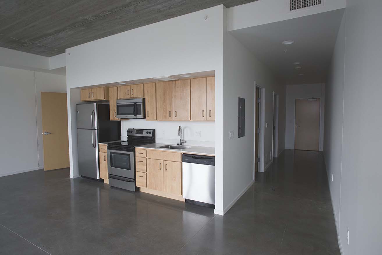 Interior image of galley style kitchen and interior hallway leading to entry.