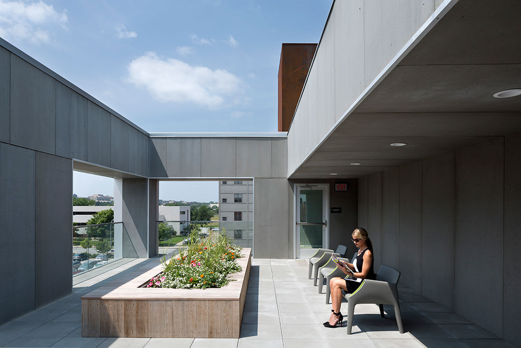 Exterior image of the roof-top common areas. A tenant sits in the shade reading, while the sun warms the courtyards many seating areas.